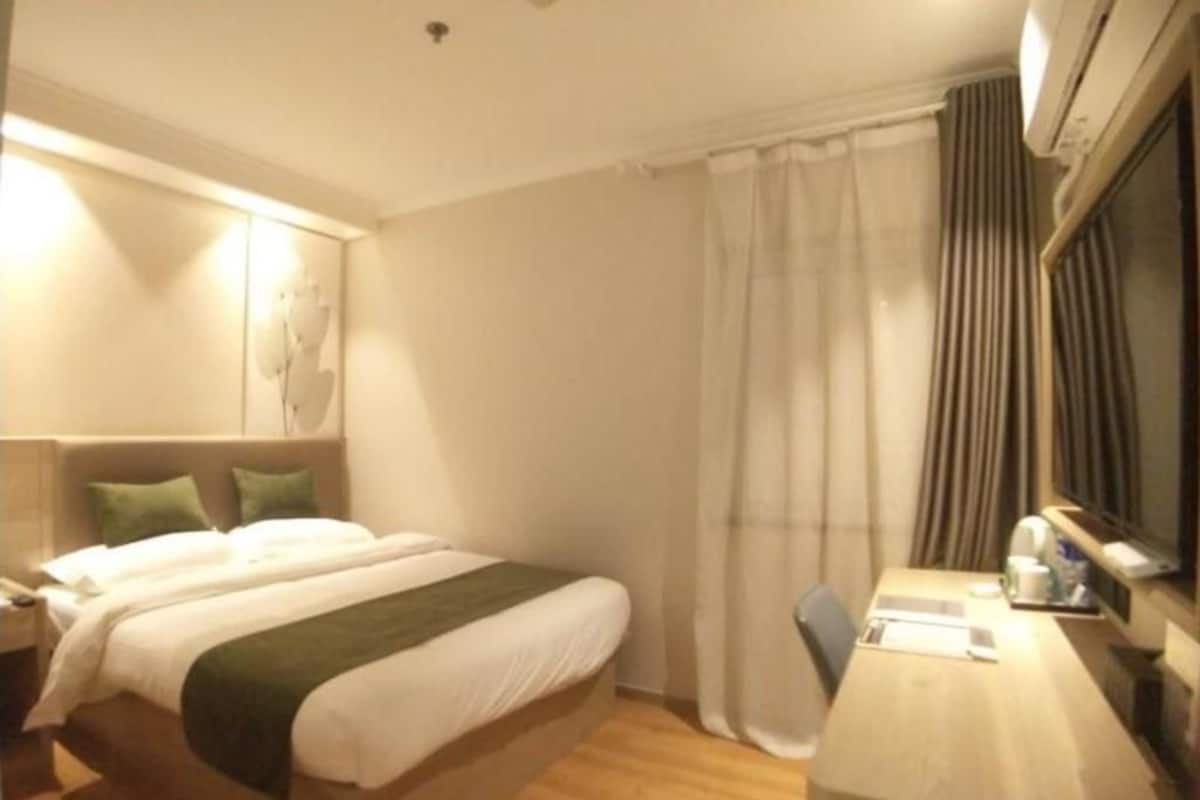 Habitación de hotel con cama, escritorio, silla y ventana con cortinas.