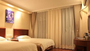 Ett hotellrum med två sängar, ett trägolv, ett skrivbord med en lampa och en tavla på väggen.
