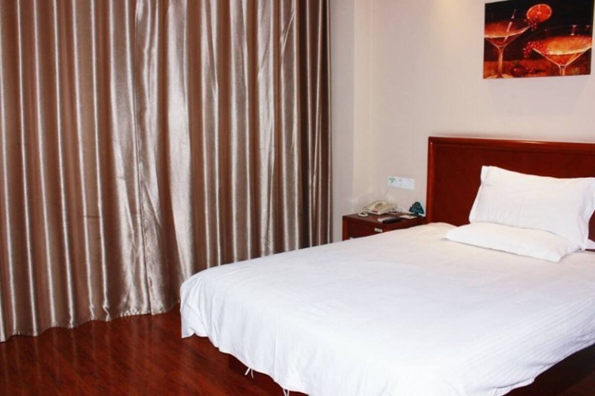 A hotel room with a large bed, a wooden headboard, a nightstand with a phone, and a painting on the wall.