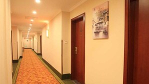 En hotellkorridor med ett mattbeklätt golv, trädörrar och en tavla på väggen.