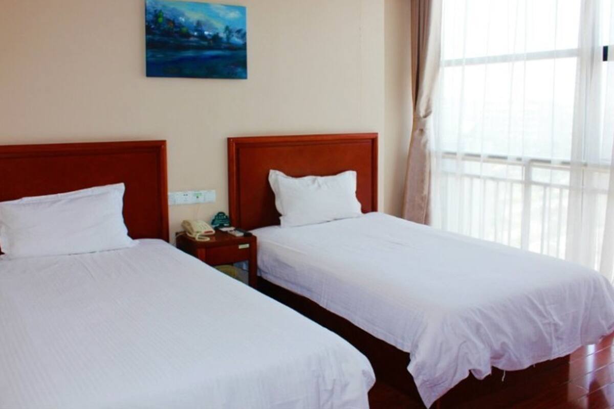 A hotel room with two single beds, a nightstand with a telephone, and a painting on the wall.