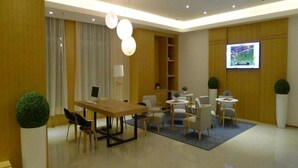 Ein modernes Hotelzimmer mit Holzboden, einer Essecke mit Tisch und Stühlen, einem an der Wand montierten Fernseher und einem großen Fenster mit Vorhängen.