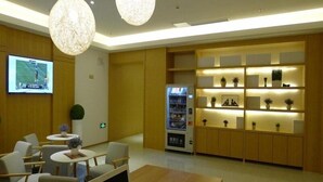 Eine moderne Hotellobby mit Sitzgelegenheiten, einem Fernsehbildschirm, einem Automaten und einem gut beleuchteten Empfangsbereich.