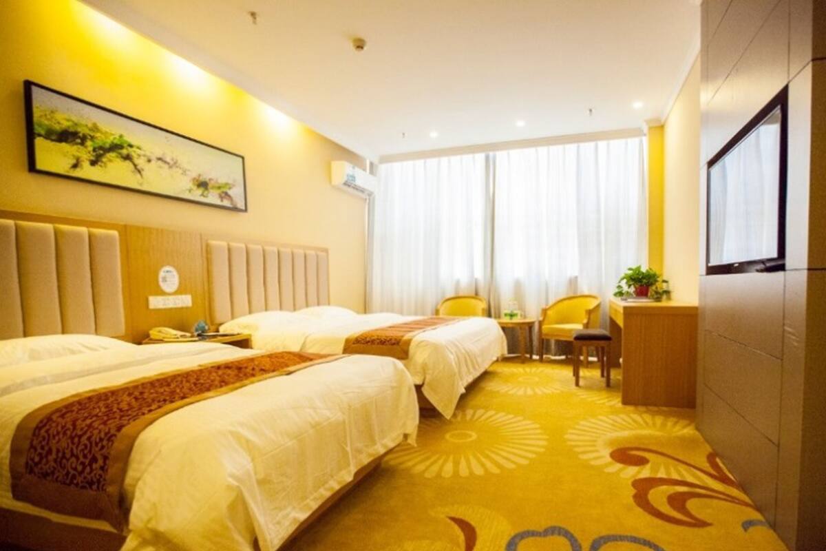 A hotel room with two beds, a desk, a chair, and a large window with curtains.