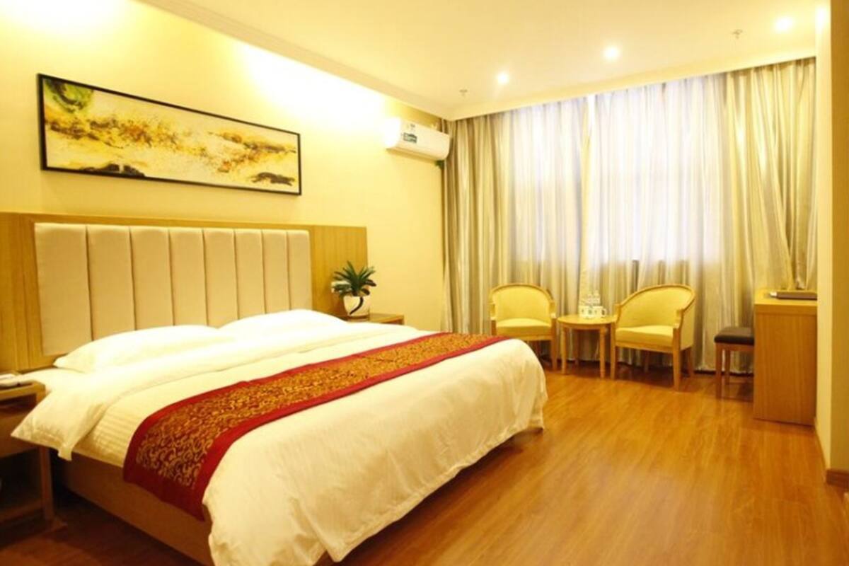 A hotel room with a large bed, a small table, two chairs, a potted plant, and a painting on the wall.
