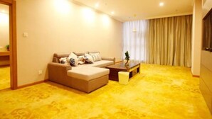A living room with a beige sofa, a coffee table, and a yellow patterned carpet. - GreenTree Inn Yancheng Dongtai Huiyang Road Guofu Hotel (Yancheng)