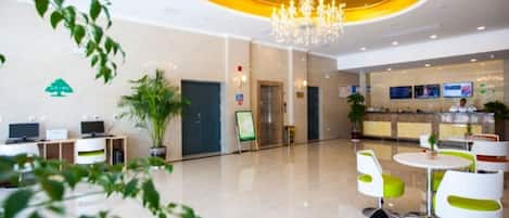 Un moderno vestíbulo de hotel con una araña, mostrador de recepción, zona de estar y una planta verde.