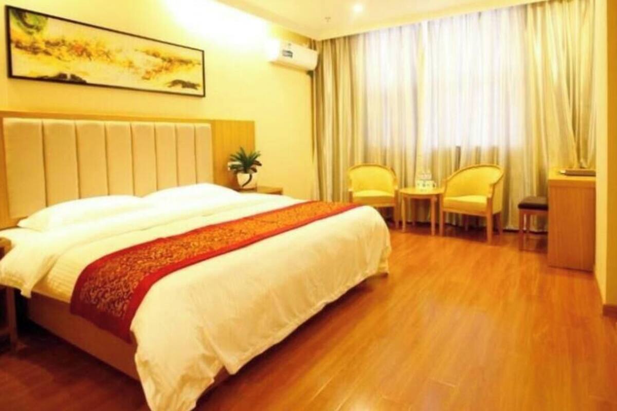A hotel room with a large bed, a bedside table, a chair, a small table, and a window with curtains.