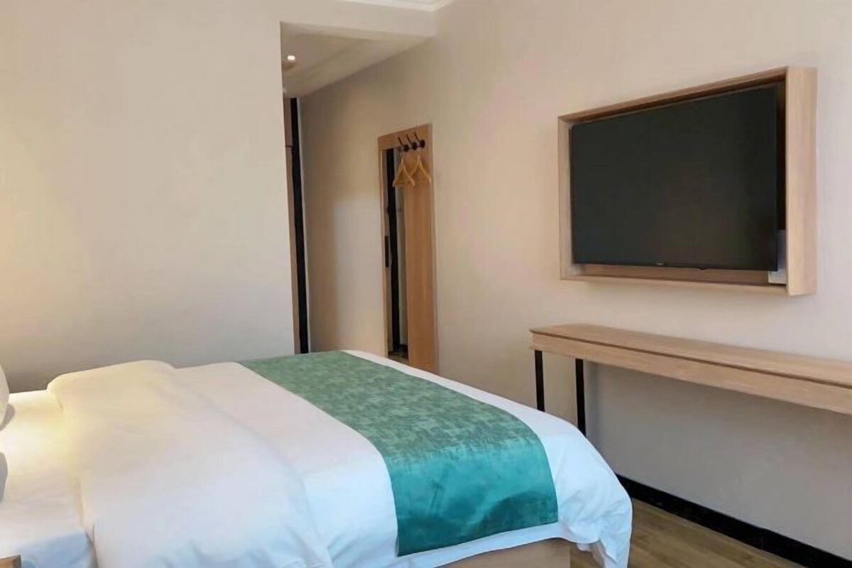 Une chambre d’hôtel avec un lit, un téléviseur fixé au mur et un banc en bois.