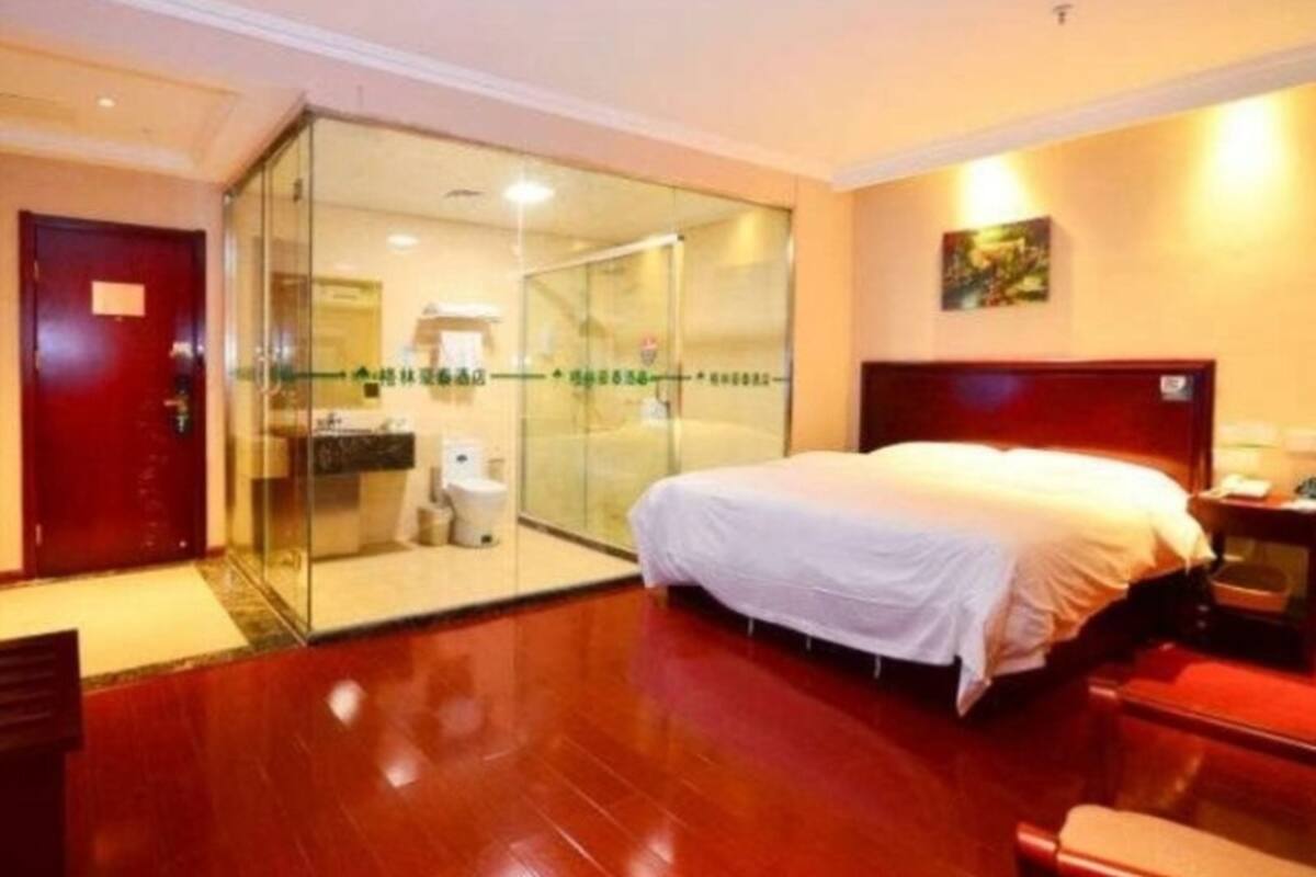 Ein Hotelzimmer mit Bett, Schreibtisch, Stuhl, Badezimmer und einer Glastür, die auf einen Balkon führt.