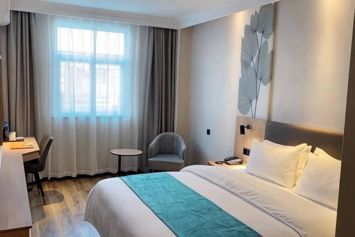 Ein Hotelzimmer mit Bett, Schreibtisch, Stuhl, kleinem Tisch und einem Fenster mit Vorhängen.