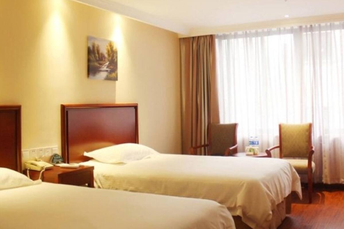 Ein Hotelzimmer mit zwei Betten, einem Nachttisch mit Telefon, einem Sessel und einem Fenster mit Vorhängen.