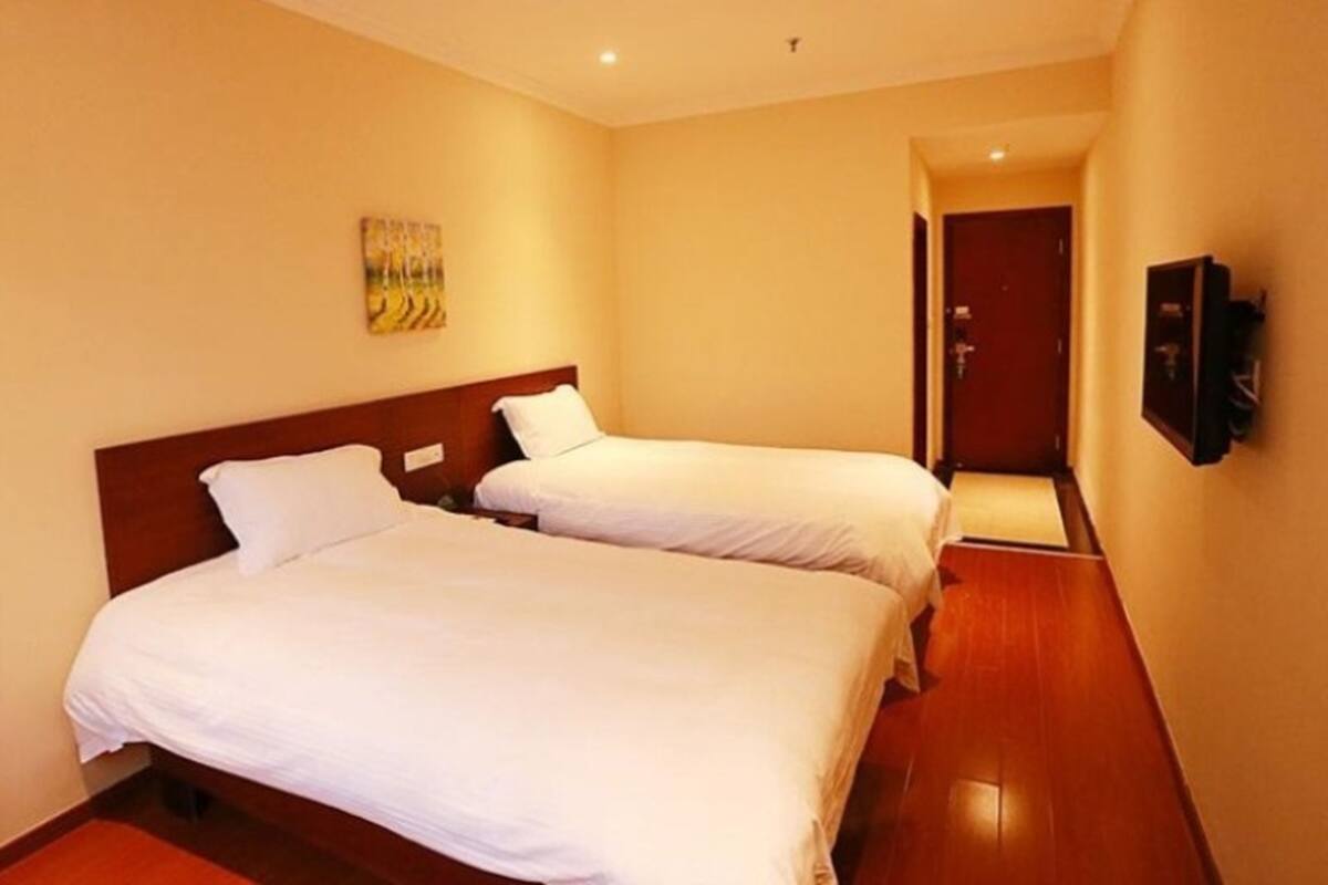 Ein Hotelzimmer mit zwei Einzelbetten, einem Holzkopfteil, einem Bild an der Wand und einer Tür zu einem anderen Raum.