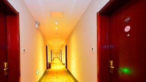 Een hotelgang met tapijtvloeren, houten deuren en een lange corridor die uitkomt in een heldere ruimte.