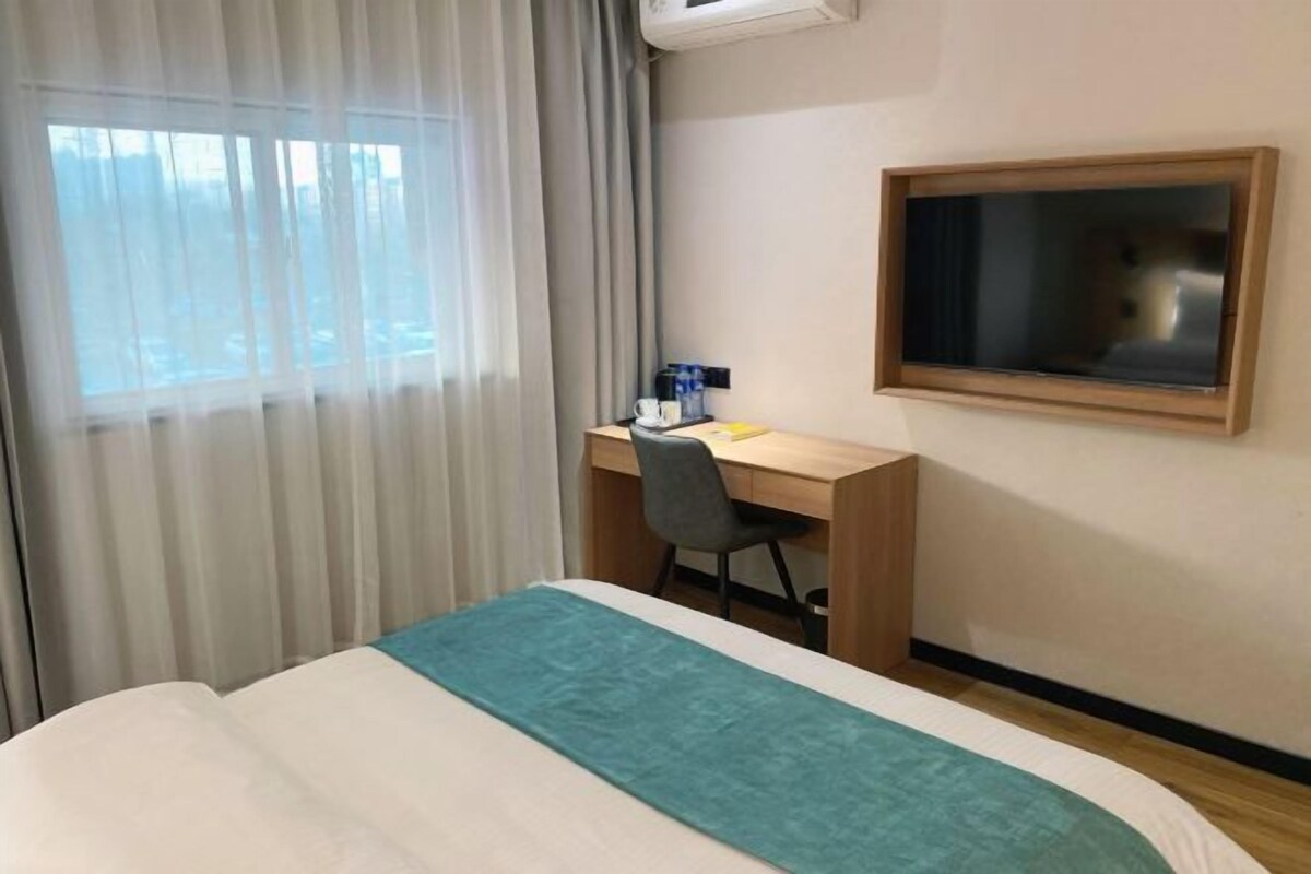 Une chambre d’hôtel avec un lit, un bureau, une chaise, une télévision et une fenêtre avec des rideaux.
