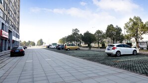 Un parking avec plusieurs voitures, un immeuble à étages doté de nombreuses fenêtres et un ciel dégagé avec quelques nuages.