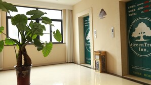 Un hall d’hôtel avec une grande plante en pot, une fenêtre avec des rideaux et une enseigne GreenTree Inn.