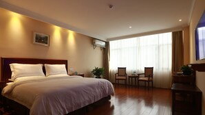 Une chambre d’hôtel avec un grand lit, une petite table avec des chaises, une plante en pot et une fenêtre avec des rideaux.
