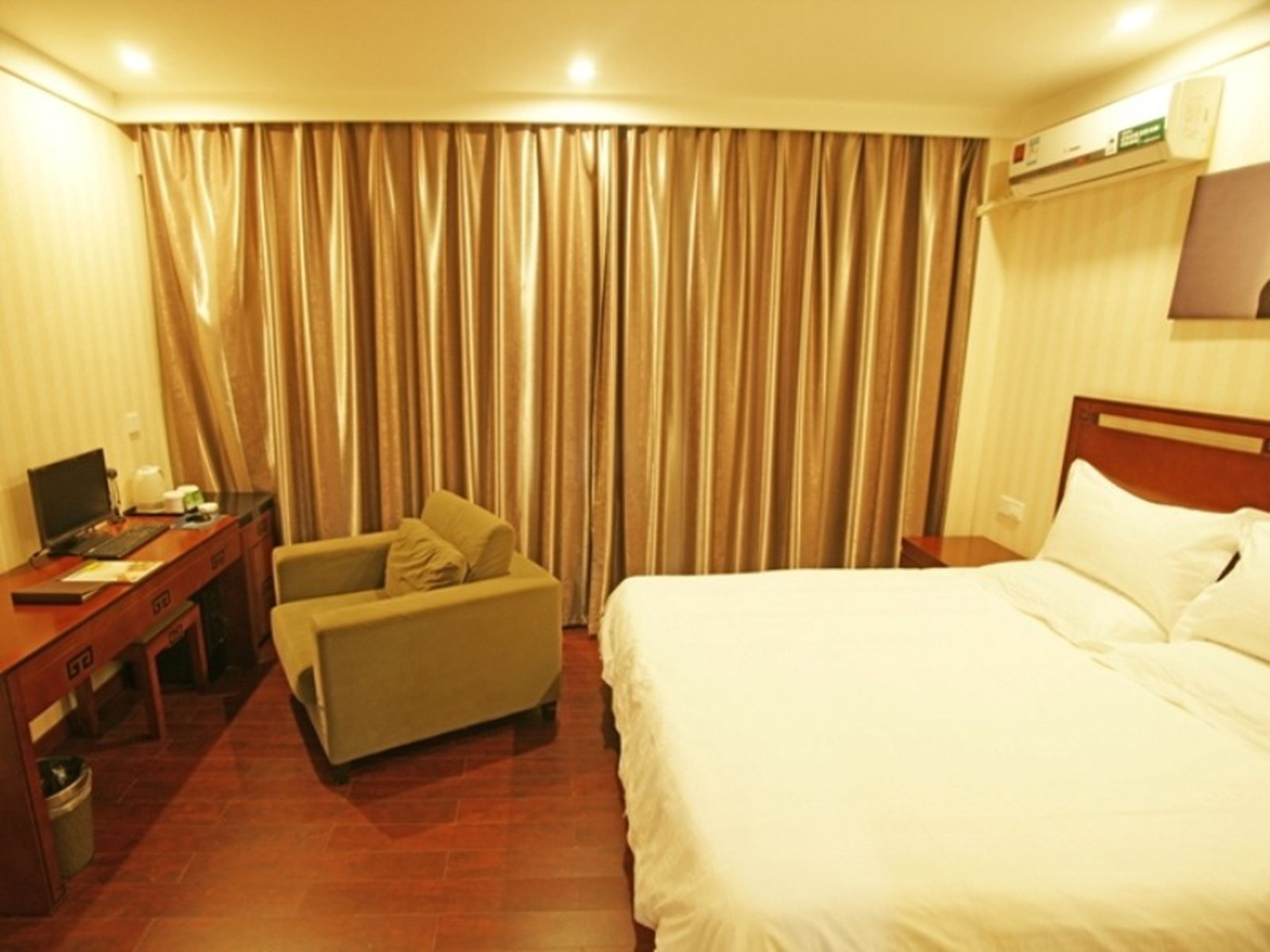 Habitación de hotel con cama, escritorio con computadora, silla y ventana grande con cortinas.