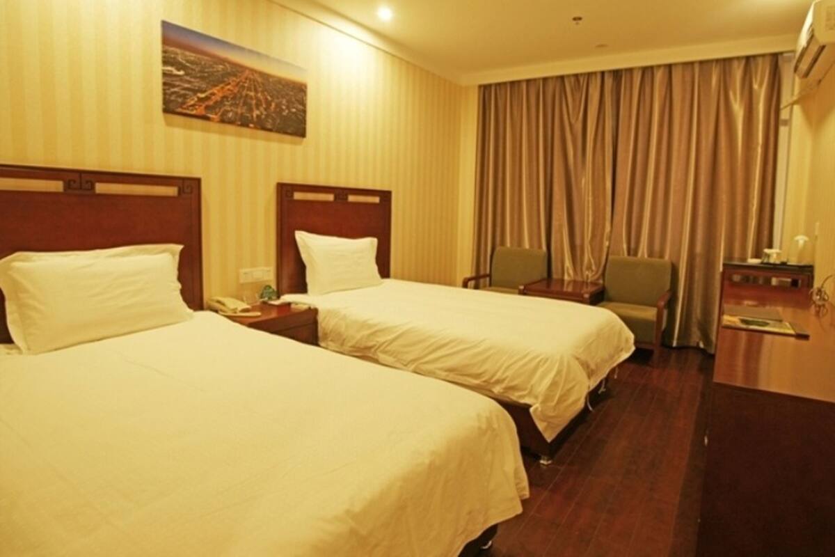 A hotel room with two beds, a nightstand, a chair, and a large window with curtains.