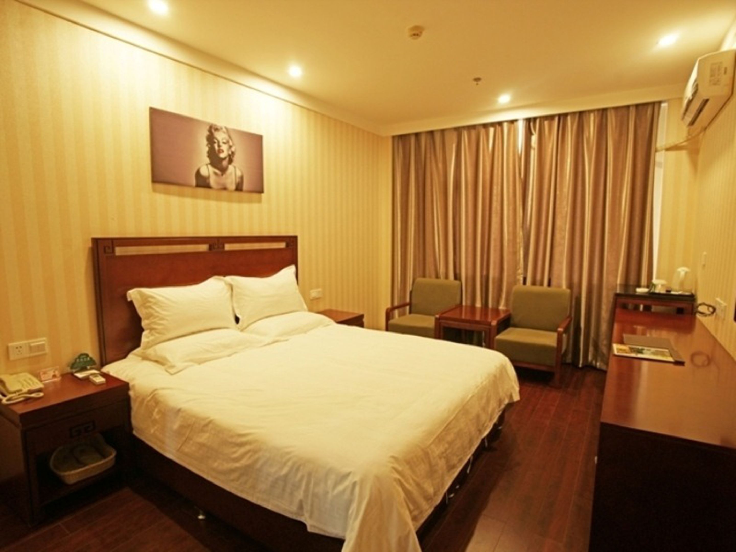 Ein Hotelzimmer mit einem großen Bett, einem Nachttisch mit Telefon und Mülleimer, einem Schreibtisch mit Stuhl und einem großen Fenster mit Vorhängen.