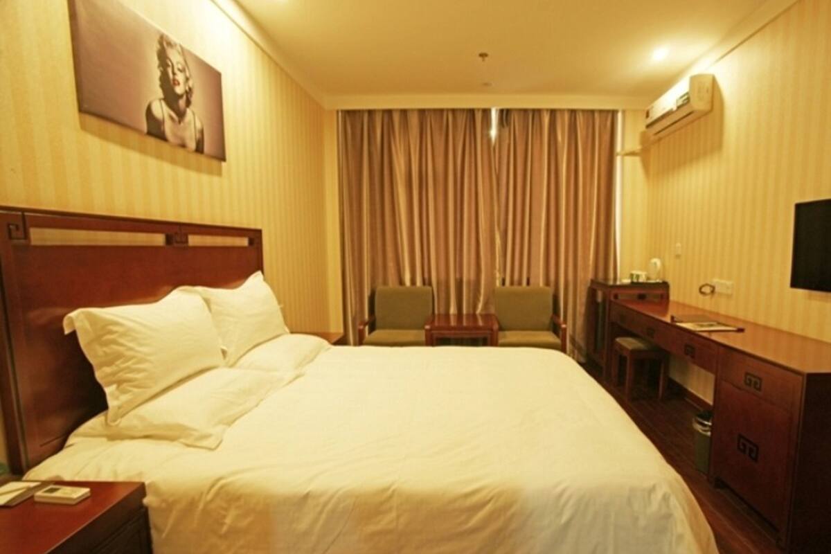 A hotel room with a large bed, a desk, a chair, and a television.