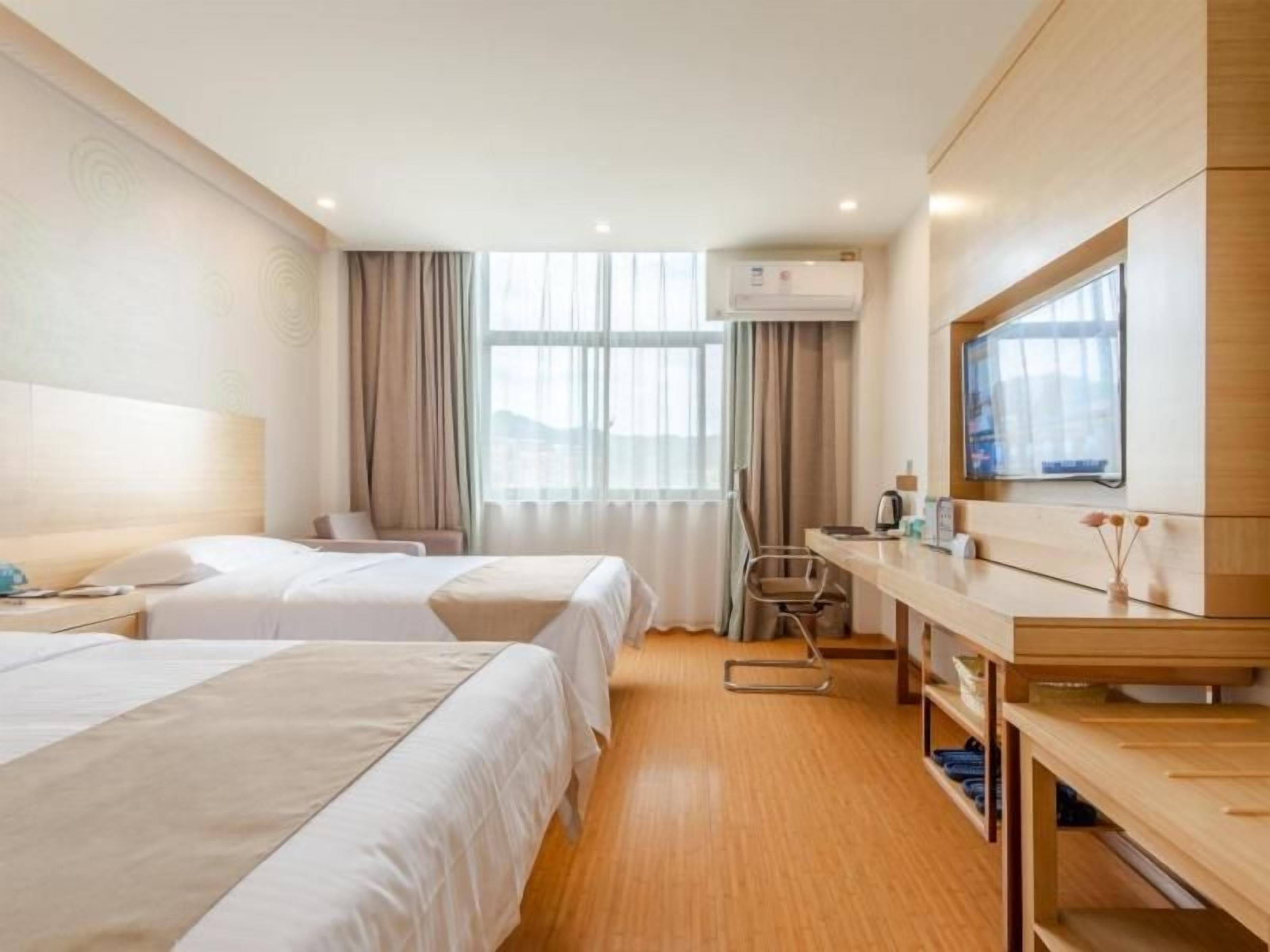 A hotel room with two beds, a desk, a chair, a television, and a window with curtains.
