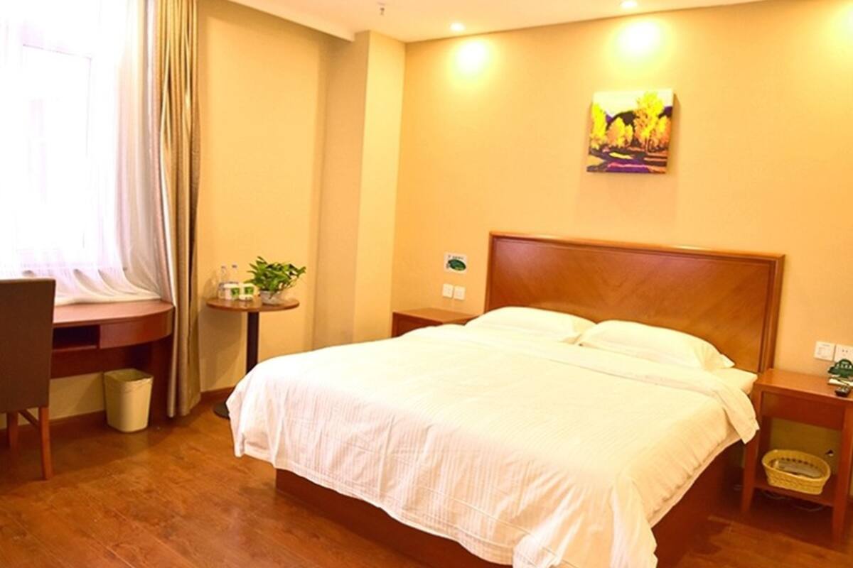 A hotel room with a large bed, wooden headboard, bedside tables, a desk, and a window with curtains.