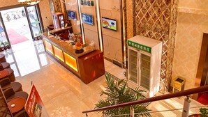 A hotel reception area with a reception desk, a digital screen, and a glass elevator. - GreenTree Inn BaoDing Xiong county XiongZhou Road Express Hotel (Baoding)