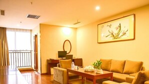 A hotel room with a wooden floor, a sofa, a coffee table, a desk with a computer, a mirror, and a painting on the wall. - GreenTree Inn BaoDing Xiong county XiongZhou Road Express Hotel (Baoding)