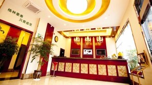 A hotel reception area with a modern design, featuring a circular ceiling light, a reception desk with a red and gold color scheme, and a large window providing natural light. - GreenTree Inn TaiZhou XianJu Passenger Center West HuanCheng Road Express Hotel (Taizhou)
