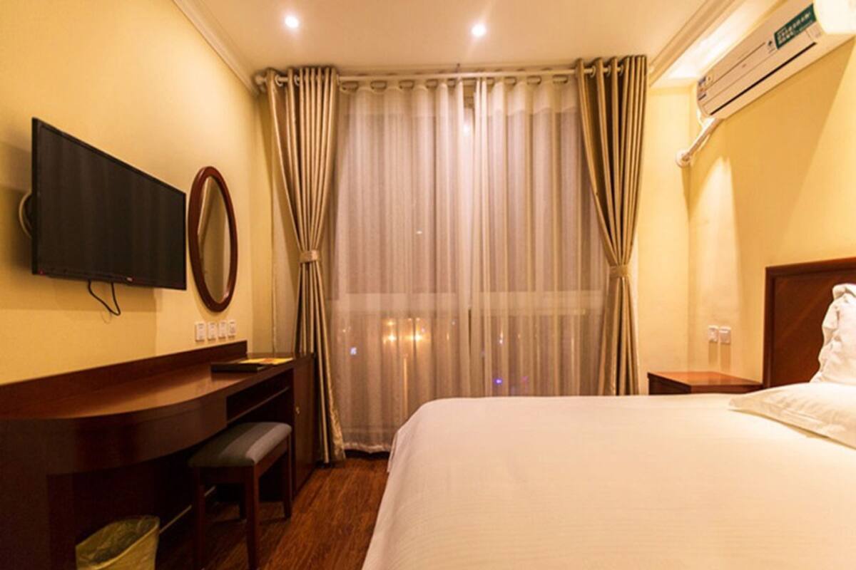 Una habitación de hotel con cama, escritorio con silla, televisor y ventana con cortinas.