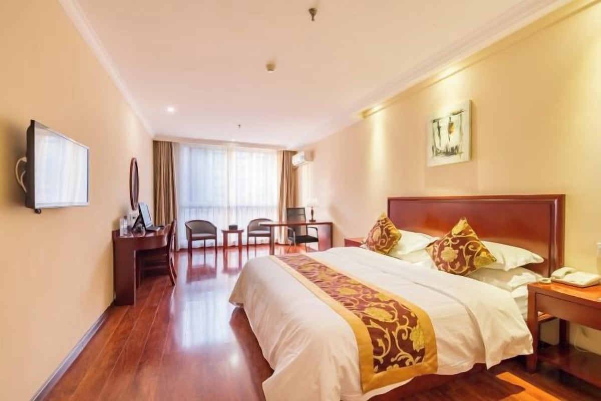 Una habitación de hotel con una cama grande, un escritorio con silla, un televisor y una ventana con cortinas.