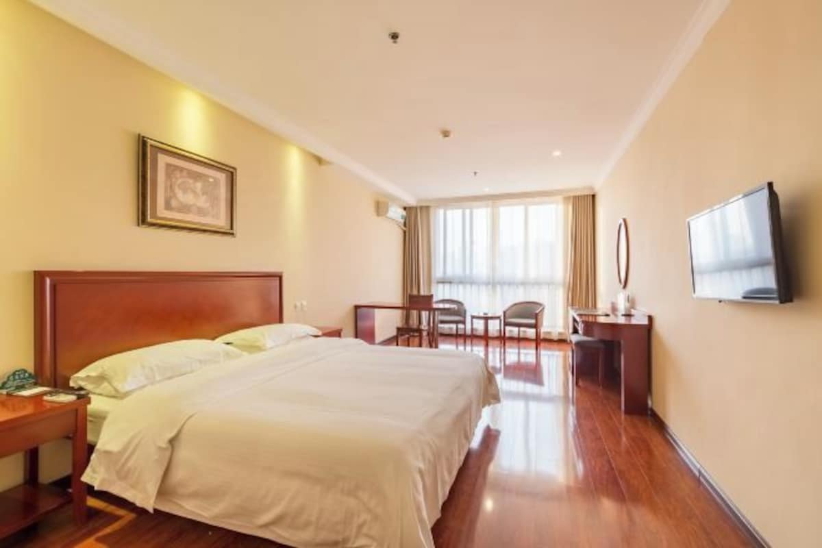 Een hotelkamer met een groot bed, nachtkastjes, een bureau met stoel, een televisie en een raam met gordijnen.