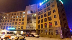 A hotel with multiple floors, a large entrance, and a parking area with several vehicles.