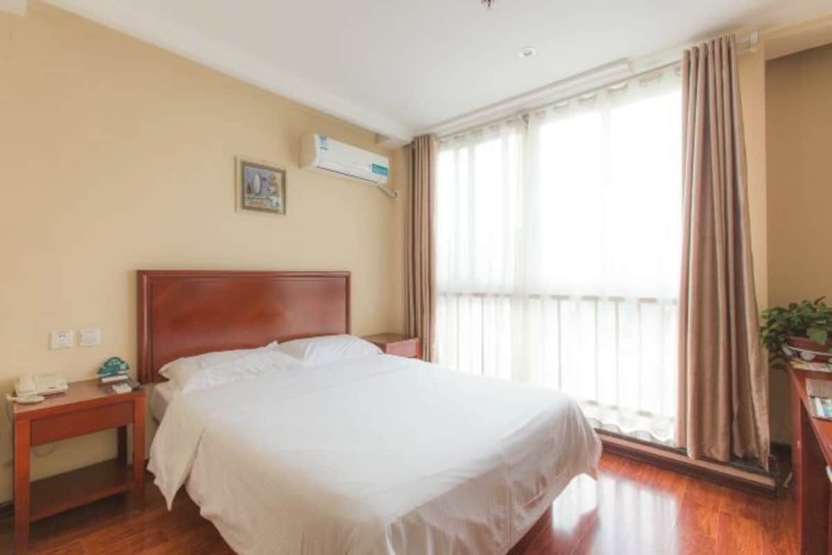 Een hotelkamer met een houten bed, een nachtkastje, een wandairconditioner en een raam met gordijnen.