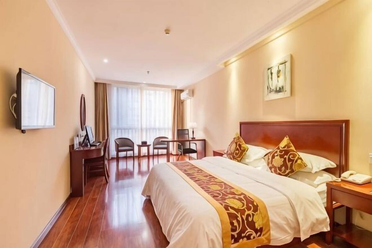 Habitación de hotel con una cama grande, un escritorio con silla, un televisor y una ventana con cortinas.