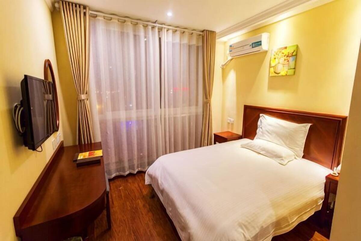 Habitación de hotel con cama, televisión, escritorio, ventana con cortinas y aire acondicionado.