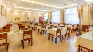 A hotel dining area with multiple tables and chairs, a clock on the wall, and a window with curtains.