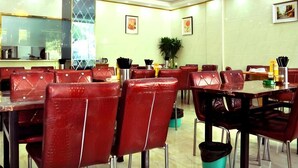 Un restaurante con sillas y mesas de cuero rojo, un pilar central y cuadros en las paredes.