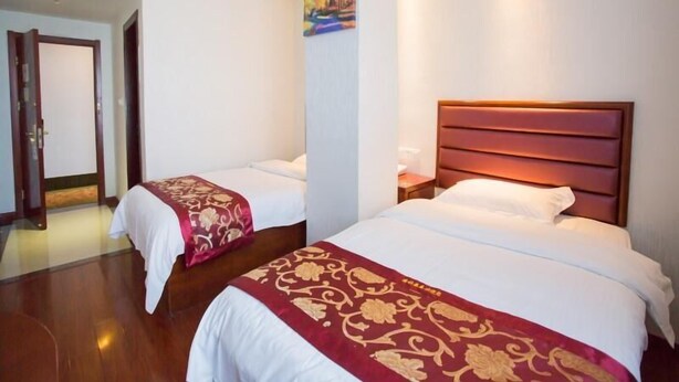 Habitación de hotel con dos camas, cada una con cubrecama rojo y dorado, cabeceros de madera y un cuadro en la pared.