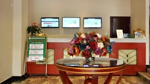 Un área de recepción con una mesa de vidrio, un centro de mesa floral y tres monitores en la pared.
