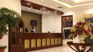 A reception area with a wooden reception desk, a large potted plant, and a decorative vase with flowers.