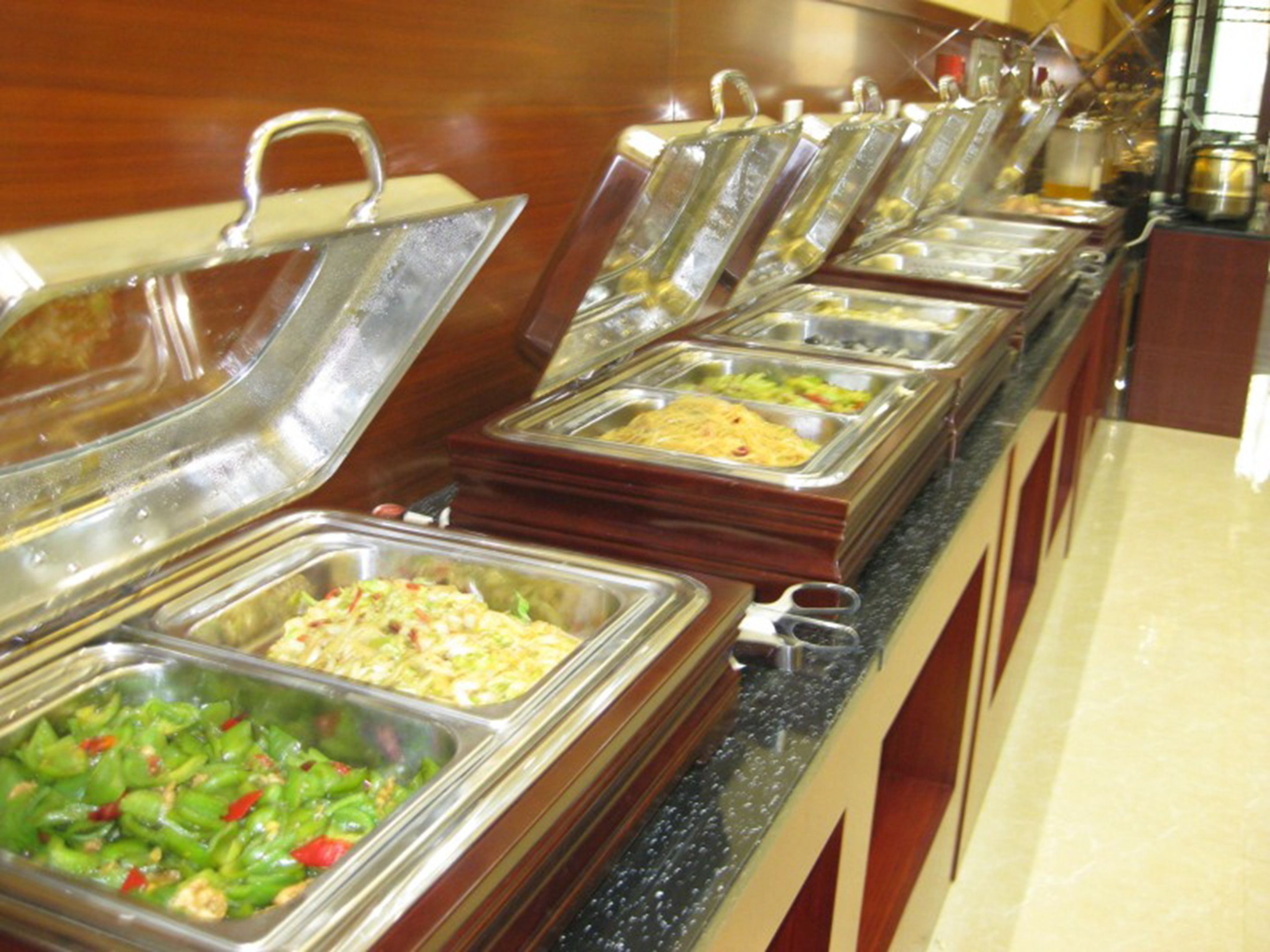 A buffet with various food items in metal containers, arranged on a counter with a wooden backdrop.