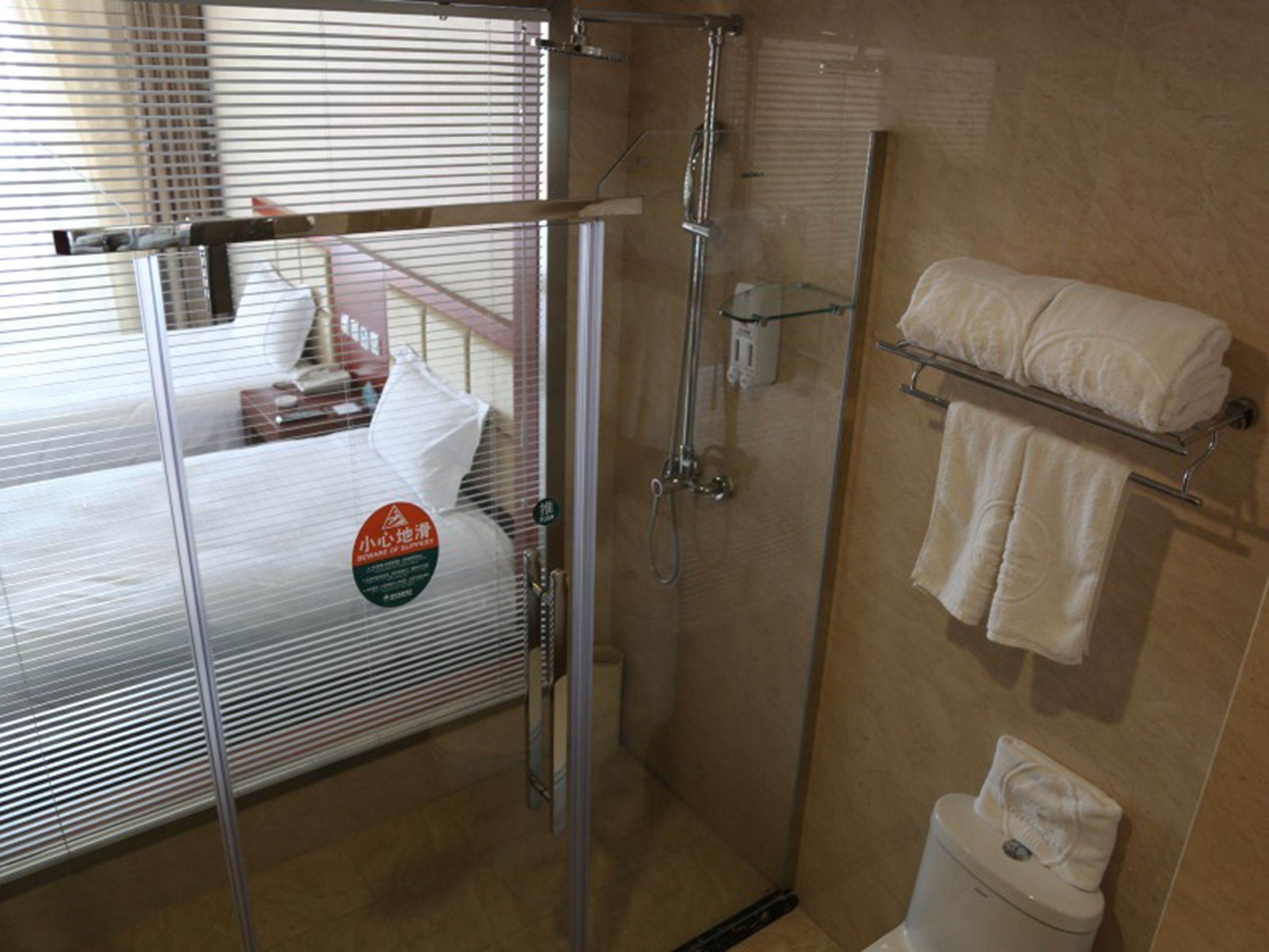 Un baño de hotel con cabina de ducha de vidrio, un inodoro y un perchero con toallas.
