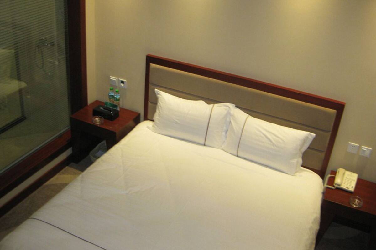 A hotel room with a large bed, a bedside table with a phone, and a glass partition.