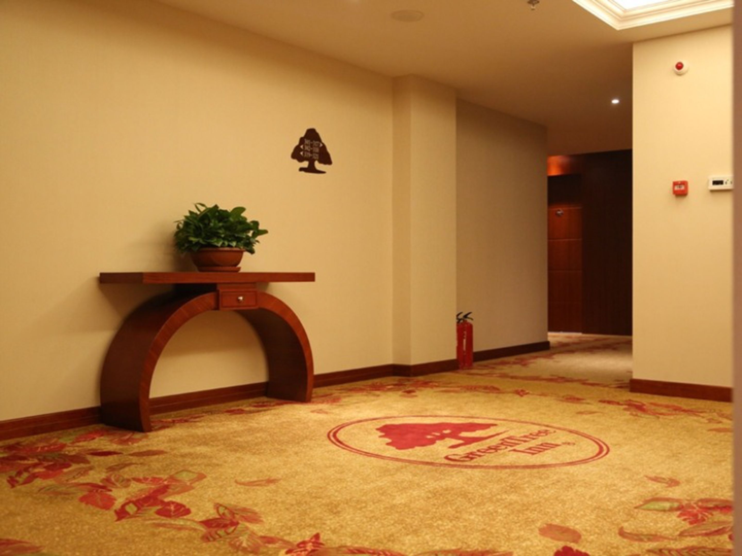 A hotel lobby with a floral carpet, a reception desk, a potted plant, and a fire extinguisher.