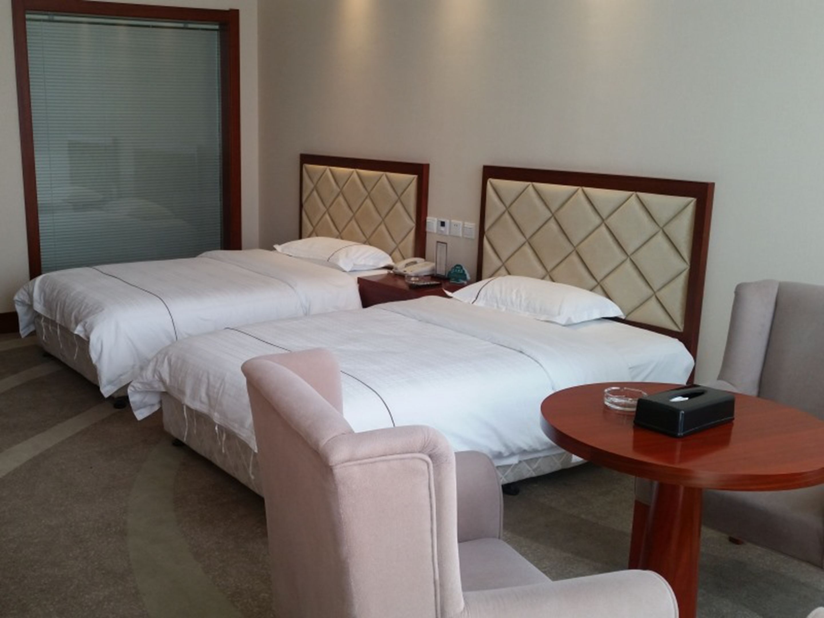 A hotel room with two beds, a small table, and a chair.