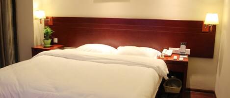 A hotel room with a large bed, two bedside tables, a nightstand, a lamp, a painting on the wall, and a small potted plant.