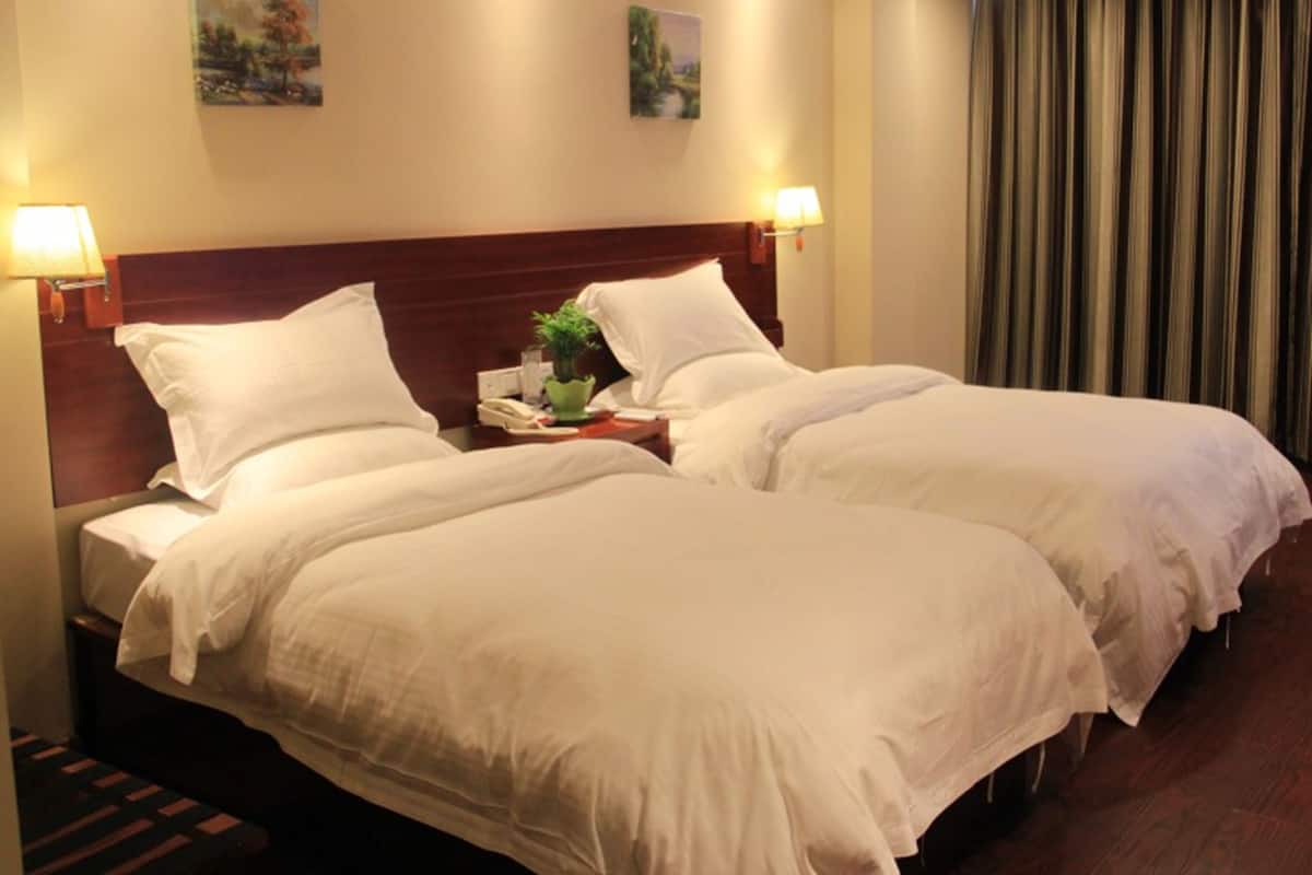 A hotel room with two beds, a wooden headboard, two wall-mounted lamps, and two paintings.